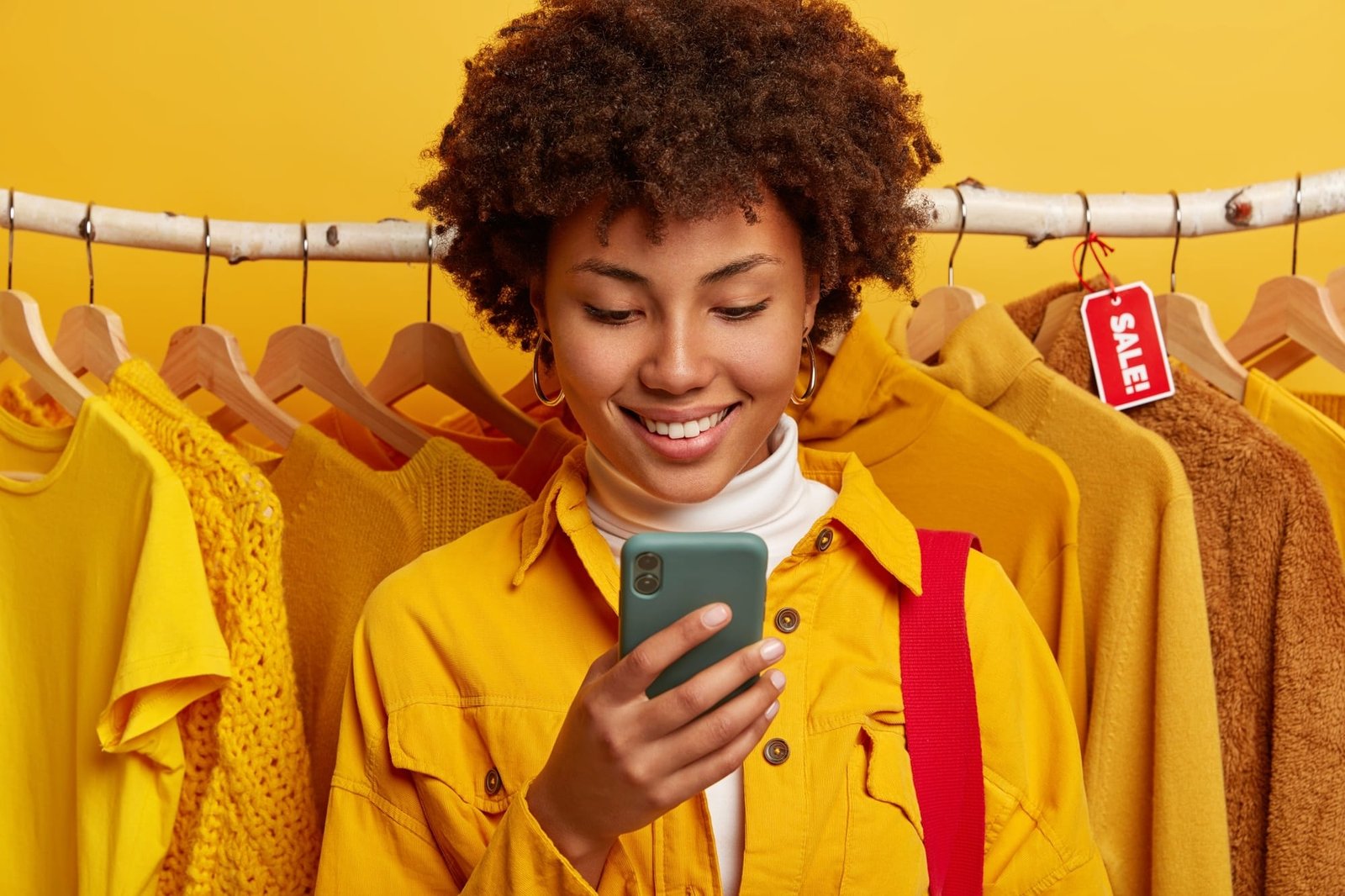 glad-online-merchant-focused-smartphone-device-stands-against-yellow-clothing-racks