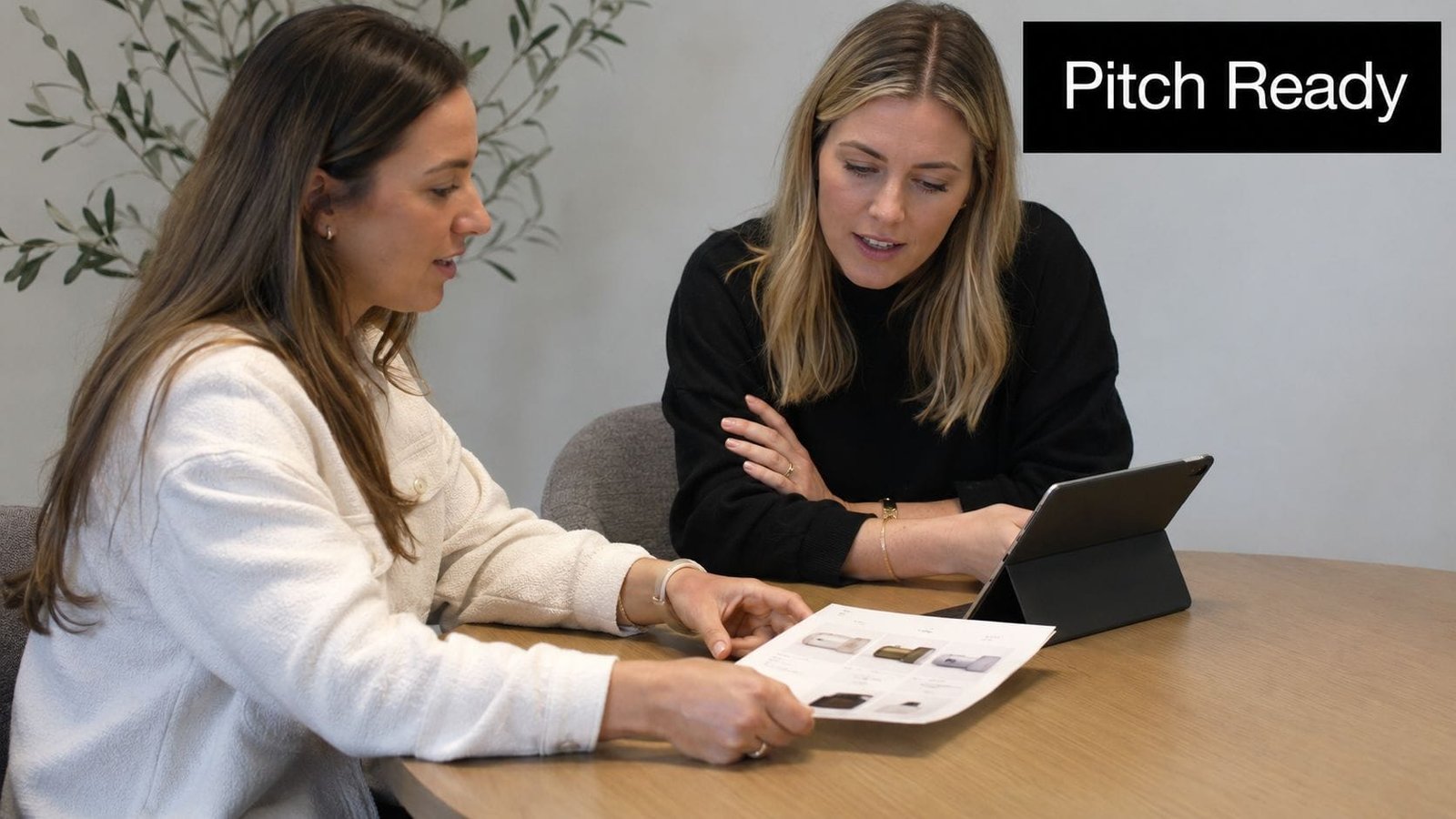 Two women collaborating on a business strategy while reviewing product photos on a document at a table.